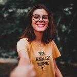 Happy woman in yellow shirt smiling broadly while enjoying the outdoors, wearing eyeglasses.