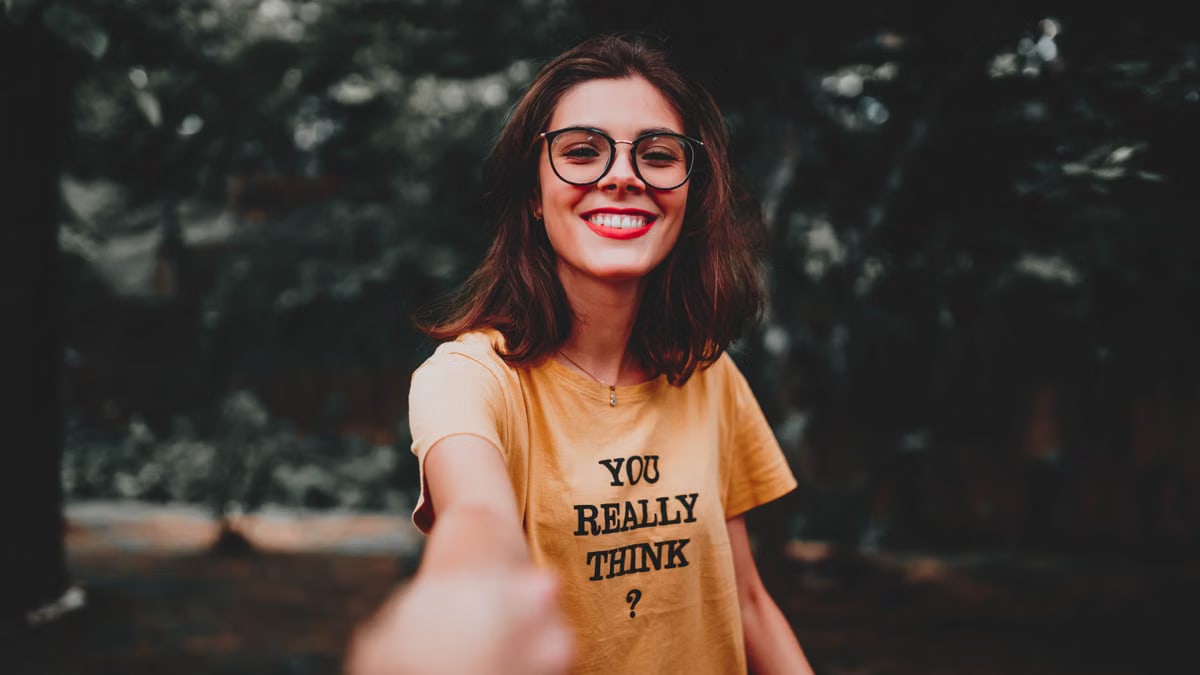 Happy woman in yellow shirt smiling broadly while enjoying the outdoors, wearing eyeglasses.